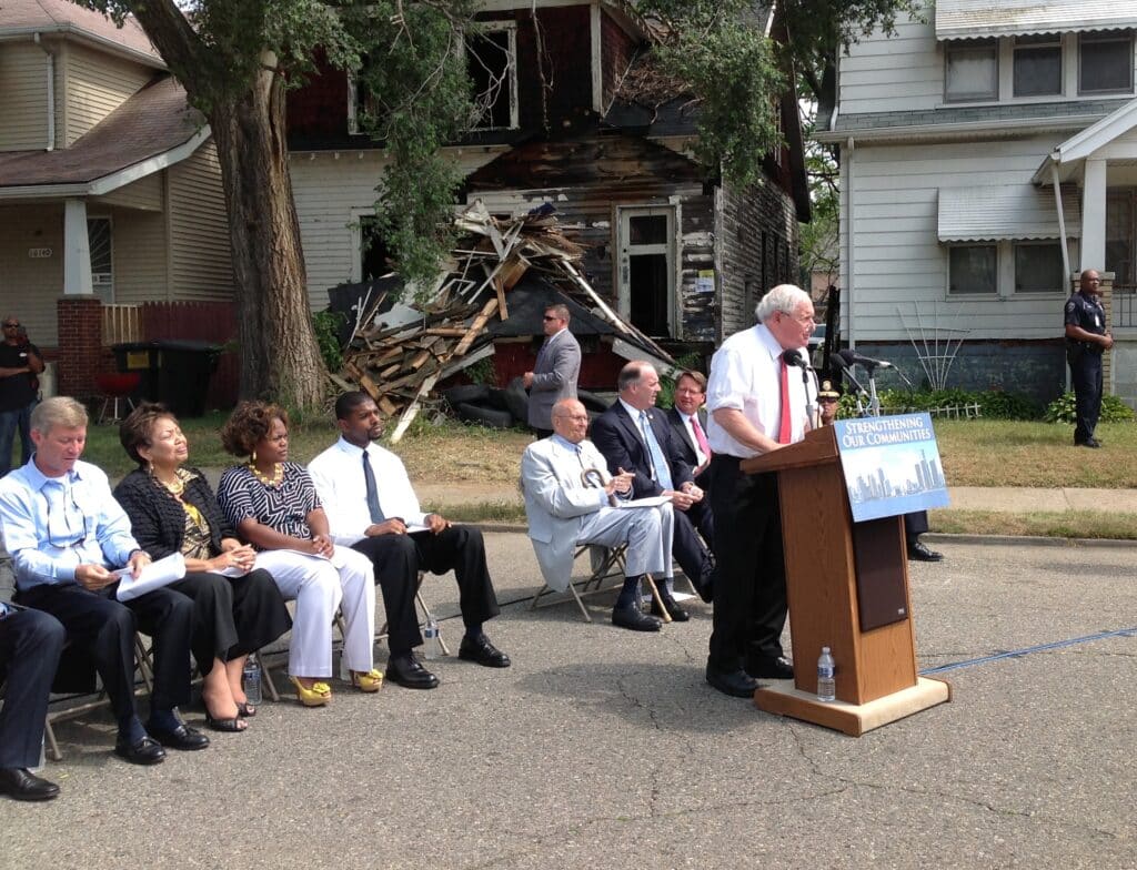 Carl Levin speaking outside in front of a brown podium.